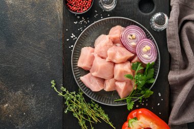 Tahtadaki tavuğun çiğ parçaları, baharatlar, otlar ve sebzeler koyu gri arka planda. Gulaş ya da şiş kebap için ham malzeme. Üst Manzara. Boş kopyalama alanı.