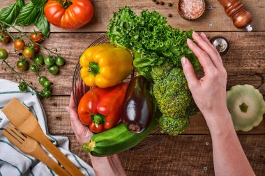 Eski ahşap arka planda taze sebzeler ve meyvelerle dolu bir sepeti tutan kadın. Mesaj için yer var. Yemek pişirme arka planı ve maketi.