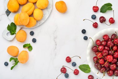 Taze kayısılar, beyaz mermer arka planda kırmızı kiraz ve böğürtlen. Vejetaryen, kilo kaybı, temiz ve sağlıklı beslenme konsepti. Üst Manzara. Boşluğu kopyala.