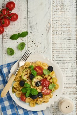 Sebzeli makarna fiocchi salatası ızgara kabak, vişneli domates, zeytin, fesleğen ve parmesan peyniri beyaz tabakta taş ya da beton arka planda. Yemek konsepti. Üst görünüm