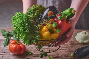 Eski ahşap arka planda taze sebzeler ve meyvelerle dolu bir sepeti tutan kadın. Mesaj için yer var. Yemek pişirme arka planı ve maketi.