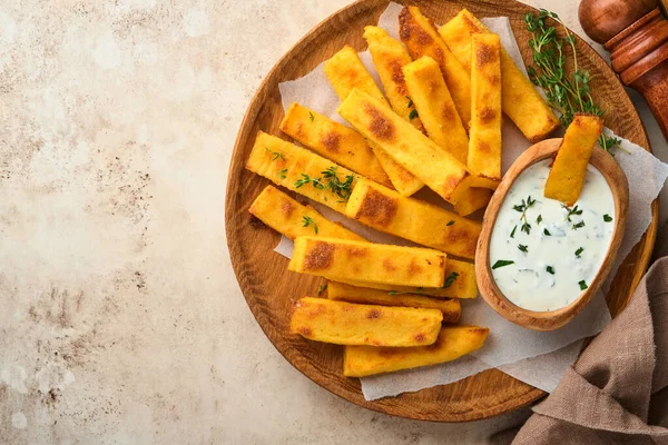 Ev yapımı polenta kızartması deniz tuzu, parmesan, kekik, yoğurt soslu biberiye. Tipik İtalyan kızarmış polentası. Kızarmış mısır çubukları. Eski aydınlık beton arka plan. Üst görünüm