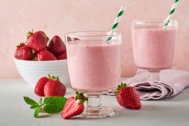 İki çilekli smoothie ya da böğürtlenli milkshake ve açık pembe arka planda nane şekeri. Yaz içeceği, milkshake ve ferahlatıcı organik konsept. Sağlıklı beslenme, vejetaryen gıda konsepti.