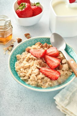 Çilek dilimli yulaf lapası, fındık bademi ve gri masadaki mavi kasede bal. Sağlıklı beslenme, diyet, vejetaryen gıda konsepti. Metin için yer