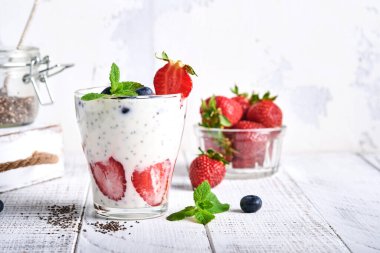 İki çilekli chia tohumu katmanlı smoothie veya açık gri arka planda çilekli ve yaban mersinli naneli milkshake. Yaz ve sağlıklı diyet içecekleri, vejetaryen gıda konsepti..