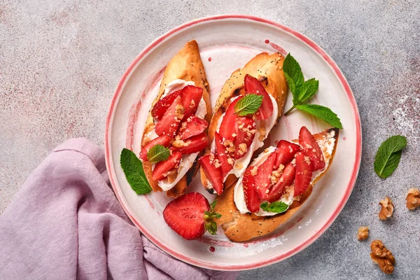 Çilekli sandviç, naneli yumuşak peynir ve açık gri taşlı arka planda seramik tabakta ceviz. Yaz ve sağlıklı diyet yemekleri, vejetaryen gıda konsepti. Üst görünüm.