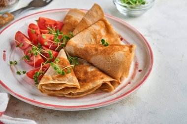 Glütensiz glütensiz karabuğday unu krep kiraz domatesli ve roka mikroyeşili beyaz tabakta, kahvaltı için ev yapımı sağlıklı pişirme. Model yap. Boşluğu kopyala.