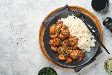 Baharatlı teriyaki tavuğu pirinçli fileto, yeşil soğanlı ve siyah susam tohumlu gri levha, taş ya da beton zemin üzerinde. Kopyalama alanı olan üst görünüm.