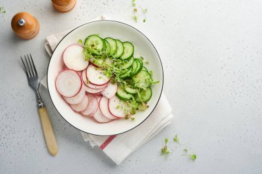 Kırmızı turplu taze salata, salatalık, sebzeler, gri taş zemin üzerinde beyaz tabakta mikroyeşil turplar. Yukarıdan bak. Vejetaryen ve sağlıklı beslenmeyi düşün..