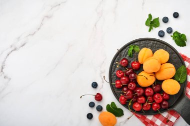 Taze kayısılar, beyaz mermer arka planda kırmızı kiraz ve böğürtlen. Vejetaryen, kilo kaybı, temiz ve sağlıklı beslenme konsepti. Üst Manzara. Boşluğu kopyala.