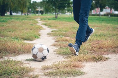 Futbol sahasında genç ayaklarıyla eski bir futbol topu. Seçici odak.