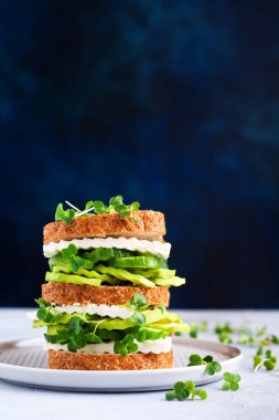 Avokado, salatalık ve beyaz peynirli sandviç. Sağlıklı bir kahvaltı için basit bir ahşap büfede mikro-yeşillik ve çok tahıllı ekmek ile süslenmiş. Seçici odak