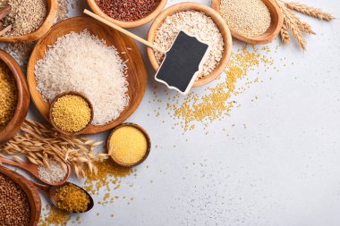 Beyaz, kahverengi ve kırmızı pirinç, karabuğday, darı, mısır Groats, kinoa ve bulgur açık gri mutfak masasında ahşap kaselerde. Glütensiz mısır gevreği. Kopyalama alanı olan üst görünüm