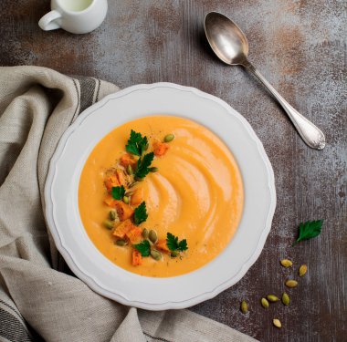 Eski bir taş veya beton zemin üzerine beyaz seramik tabak içinde ev yapımı balkabağı çorbası. Seçici odak. Üstten Görünüm. Kopya alanı.