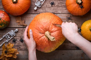Cadılar Bayramı Balkabağı. Eski ahşap arka planda Cadılar Bayramı tatili hazırlamak için balkabağı nesnesinde bıçaklı karakter yüzüyle kesen kadın ellerini işleyin. Kopya alanı olan düz sonbahar kompozisyonu