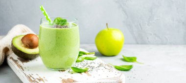 Avokado, ıspanak yaprakları, elma ve chia tohumları ve gri beton arka planda bulunan vejetaryen sağlıklı yeşil smoothie. Seçici odaklanma. Mesaj için yer var. Pankart.