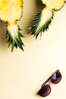 İki parçaya ayrılmış taze ananas. Sarı arka planda defter, eskiz defteri ve güneş gözlüğü. Yaz kavramı. Fotokopi alanı olan yaratıcı bir daire. Üst görünüm