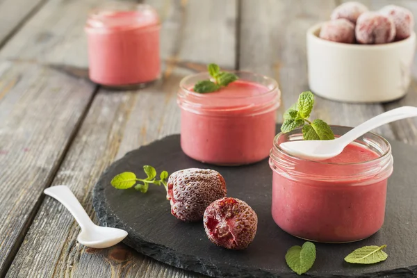 Aardbei mousse in glazen potten en bevroren aardbeien op een oude houten tafel achtergrond. Selectieve aandacht. — Stockfoto