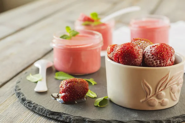 Mousse de fraises dans des bocaux en verre et fraises congelées sur un vieux fond de table en bois. . — Photo