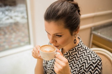 Kafedeki bir masada kahve içen bir kadının portresi.