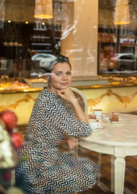 Kafede bir fincan kahve içen bir kadın. Pencereden ateş etmek.