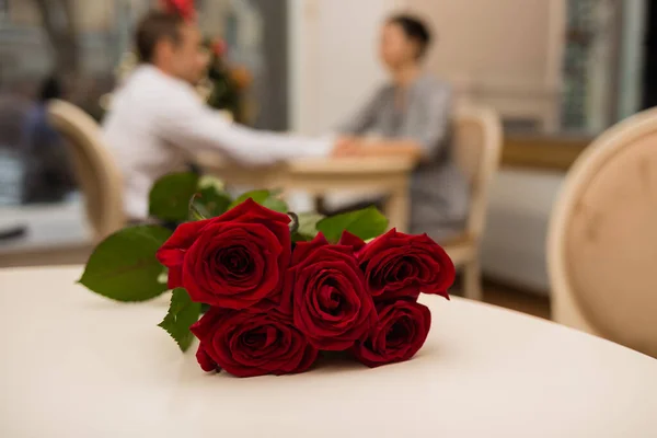 bouquet of red roses on the background of a young couple at the table