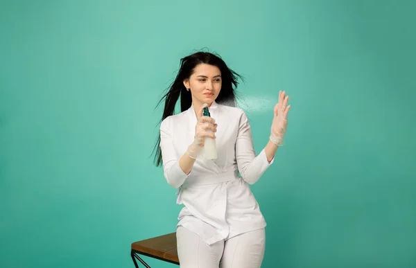 Güzellik uzmanı bir şişe tutuyor ve onu bir turkuaz arka planda havaya püskürtüyor.