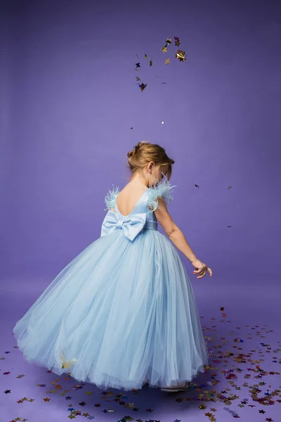 Küçük bir kız mor bir arka planda açık mavi bir elbiseyle dönüyor.
