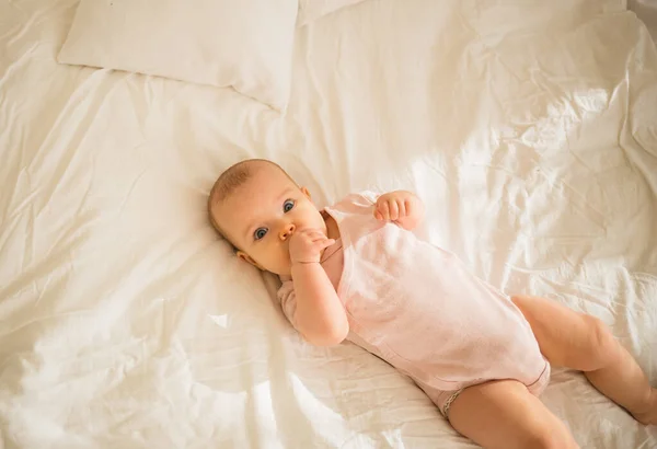 一个穿着粉色紧身衣的小女孩躺在床上的白色毛毯上 — 图库照片