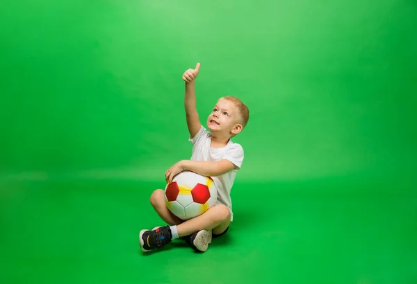 Kleine Jongen Zit Uniform Met Een Voetbal Toont Zijn Hand — Stockfoto