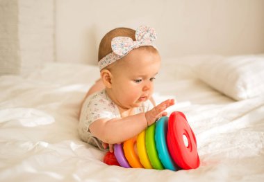 Küçük bebek siyah bir elbise ve beyaz bir battaniyenin üzerinde piramit oyuncakla yatar.