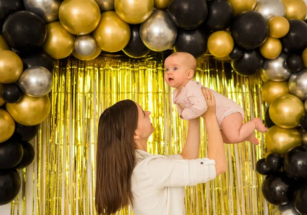 Anne bebeğini balonlarla şenlikli bir arka planda tuttu.