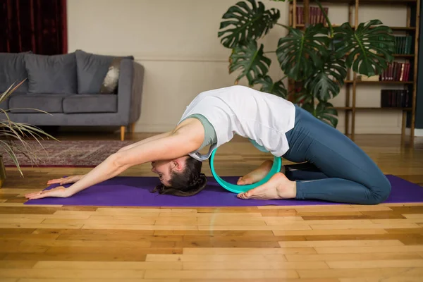 Spor üniformalı yogacı kadın evdeki bir odada paspasın üstünde tekerlekle egzersiz yapıyor.