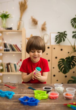 Mutlu küçük çocuk odadaki bir masada plastik ve kalıplarla oynuyor. Dikey yönelim
