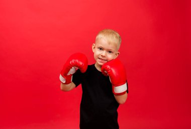 happy toddler boy boxer in red boxing gloves on red background with space for text clipart