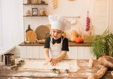 Beyaz şapkalı küçük bir aşçı ve önlüklü mutfak masasında oturur ve hamur yapar.