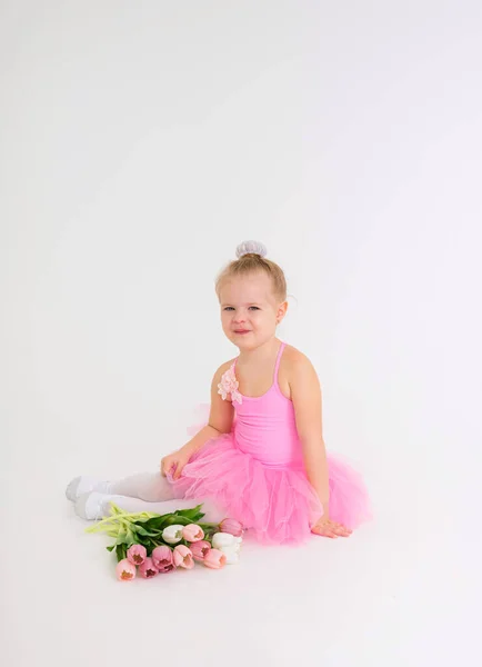 Kleines Mädchen in rosa Kleid mit Tutu-Rock sitzt mit einem Strauß bunter Tulpen und blickt in die Kamera auf weißem Hintergrund mit Platz für Text — Stockfoto