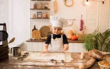 Beyaz önlüklü ve şapkalı genç bir şef ahşap bir mutfakta hamur yapıyor.