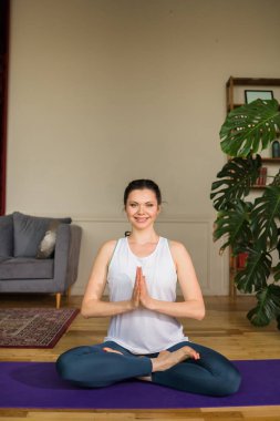 Spor giyim bölümündeki esmer kadın bir odada Padmasana Asana egzersizi yapıyor. Evde yoga.