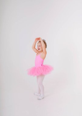 Pembe etekli küçük sarışın balerin beyaz bir arka planda dans ediyor.