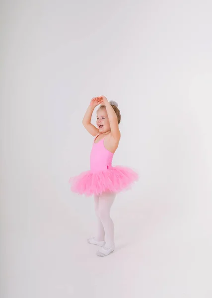 Pembe etekli küçük sarışın balerin beyaz bir arka planda dans ediyor.