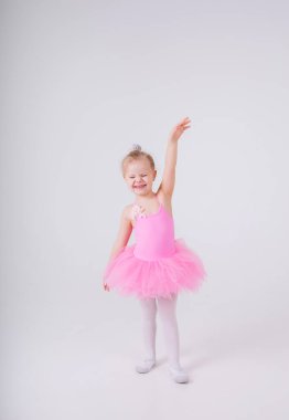 Pembe elbiseli, etekli küçük balerin kız beyaz bir arka planda uzun bir pozda duruyor ve mesaj için yer var.