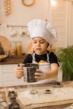 Beyaz şapkalı küçük bir aşçı ve önlük masada oturur ve mutfakta unu elemeye başlar.