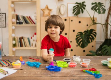 Mutlu çocuk odada plastik maddeyle bir masada oturur ve kameraya bakar.