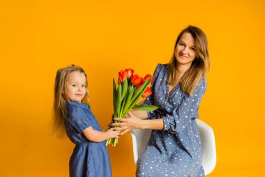 Anne ve kızı mavi elbiseli, sarı bir zemin üzerinde kırmızı laleler var ve mesaj için yer var.