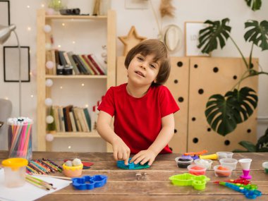 Neşeli küçük çocuk, odadaki ahşap bir masada plastikten heykel yapıyor. İnce motor becerilerin gelişimi