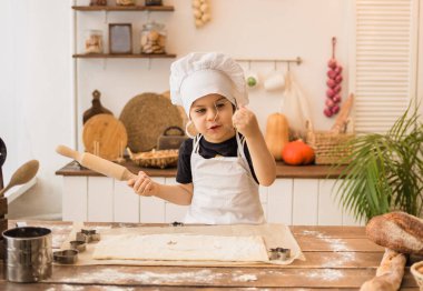 Beyaz önlüklü ve şapkalı genç aşçı ahşap bir masaya oturur ve hamuru yuvarlar.