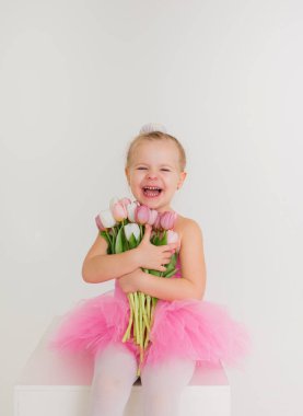 Pembe elbiseli küçük bir kızın portresi etekli beyaz arka planda bir buket lale ile oturuyor ve mesaj için yer var.