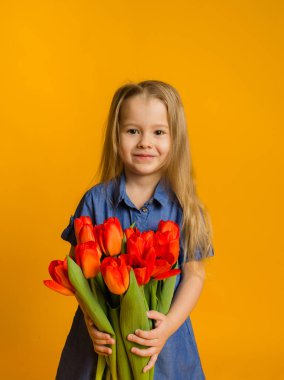 Sarışın bir kızın portresi, mavi elbiseli, ayakta duran ve sarı arka planda kırmızı lalelerle dolu bir buket tutan.