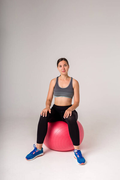 красивая девушка в спортивной форме сидит на фитнес-мяч и смотрит на камеру на белом фоне